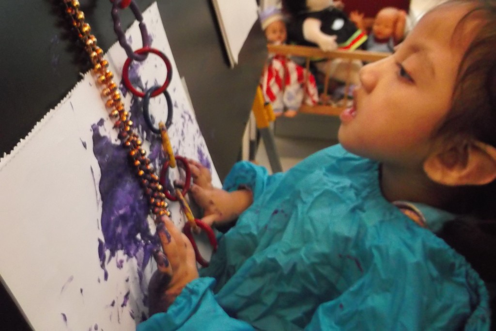 Jasmine at the paint easel. She chose purple paint today.  The beads encouraged Jasmine to look at the paper and to get her hands into the paint.